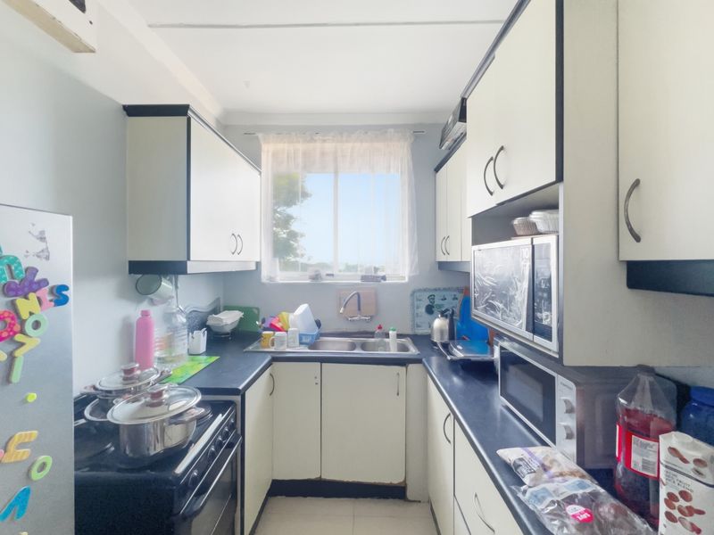 A compact galley-style kitchen featuring built-in cabinetry, laminate countertops, and a double basin sink with a window providing natural light.