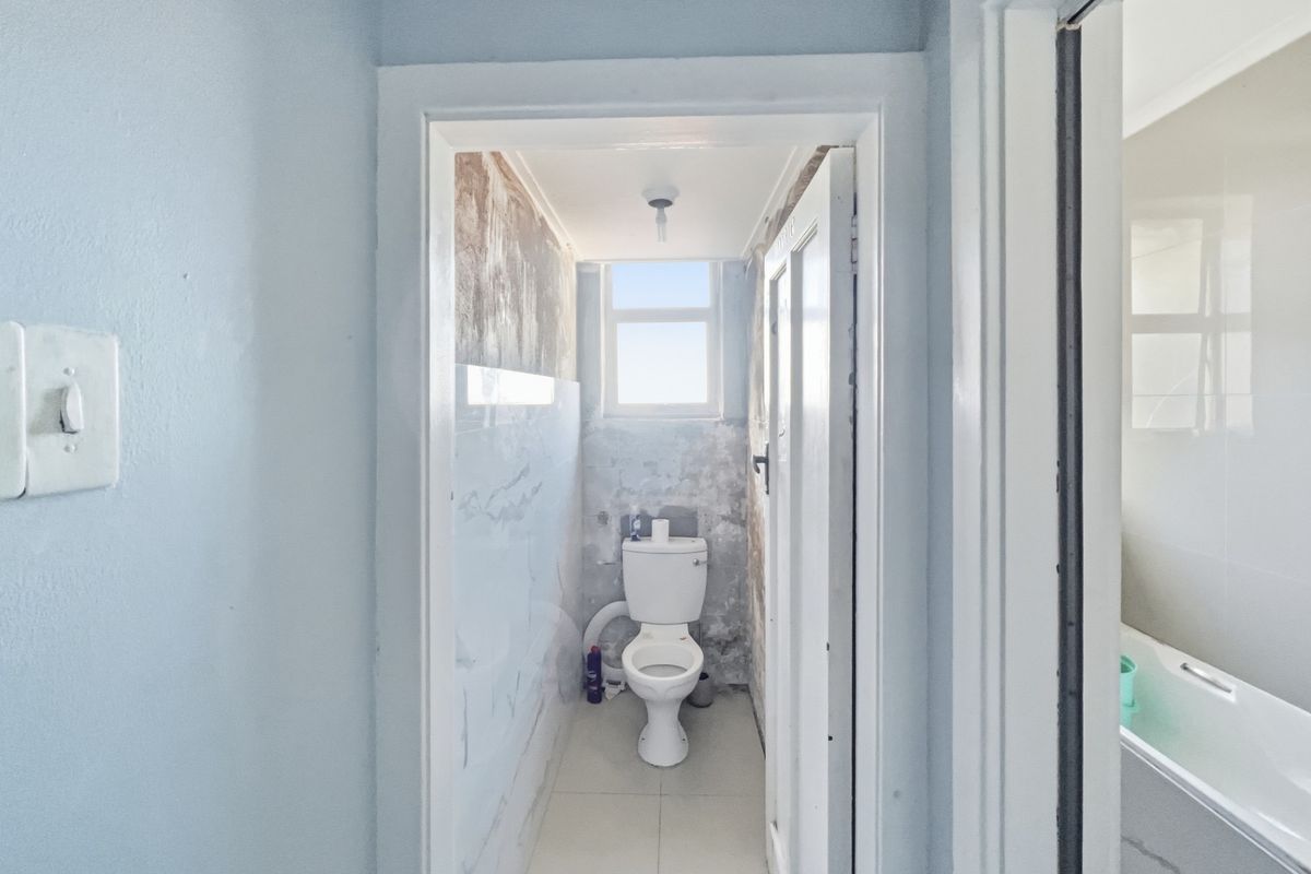 A small bathroom featuring a toilet and tiled flooring, currently requiring significant wall repairs and cosmetic updates to improve its condition.