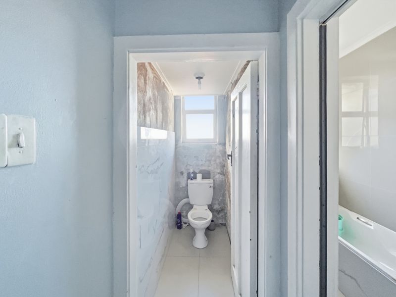 A small bathroom featuring a toilet and tiled flooring, currently requiring significant wall repairs and cosmetic updates to improve its condition.