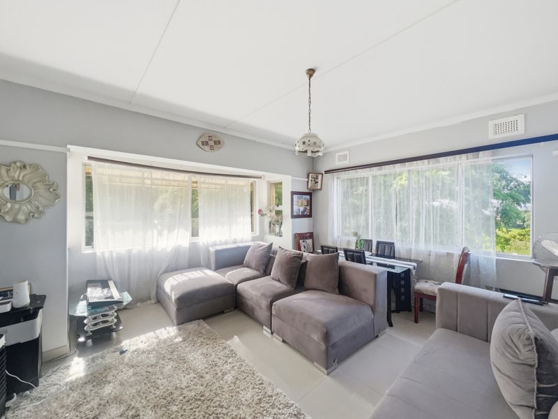 A bright, open-plan living area featuring large windows that provide ample natural light, tiled flooring, and neutral wall finishes.