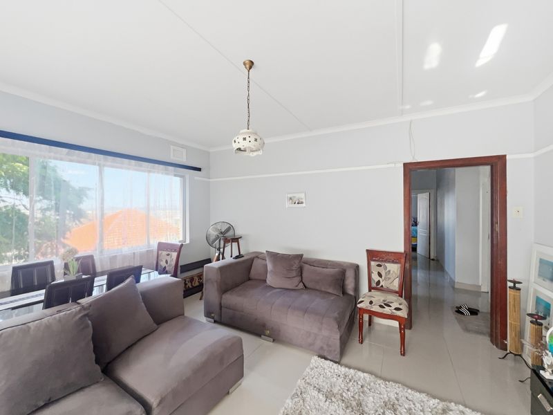 A bright living room featuring large windows, tiled flooring, and a neutral color palette, providing a comfortable and well-lit space.
