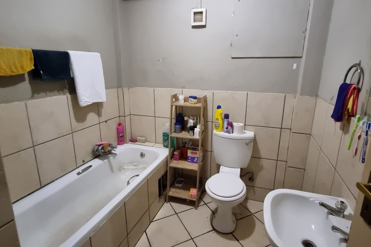 A functional bathroom featuring a standard bathtub, toilet, and pedestal basin with tiled splashbacks and flooring.