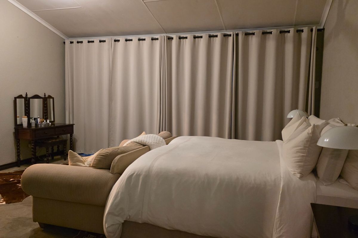 A spacious bedroom featuring a vaulted ceiling, neutral wall finishes, and large floor-to-ceiling curtains, with an adjoining bathroom visible through the doorway.