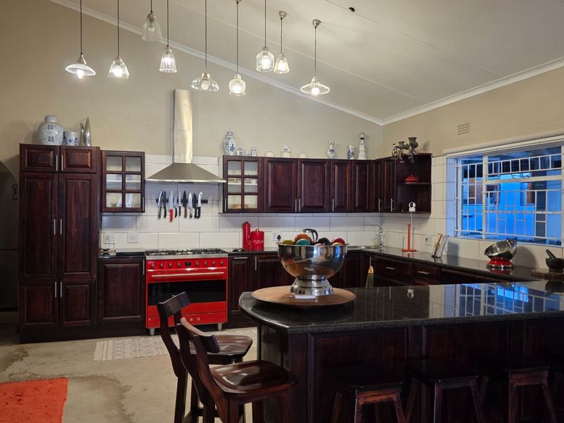 Spacious kitchen featuring dark wood cabinetry, a contrasting red range cooker, granite countertops, and a large central island with breakfast bar seating.
