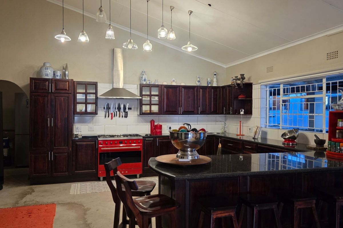 Spacious kitchen featuring dark wood cabinetry, a contrasting red range cooker, granite countertops, and a large central island with breakfast bar seating.