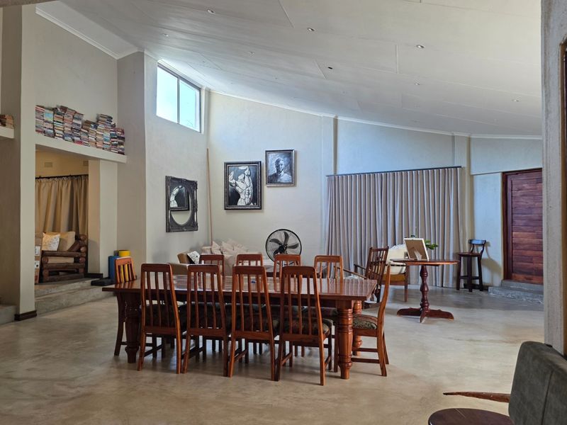Spacious open-plan living and dining area featuring high raked ceilings, polished concrete flooring, and large windows providing ample natural light.
