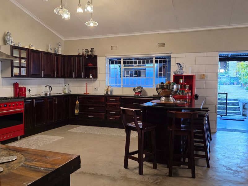 Spacious open-plan kitchen featuring dark wood cabinetry, a central island, a red Smeg range cooker, and direct access to an outdoor patio area.
