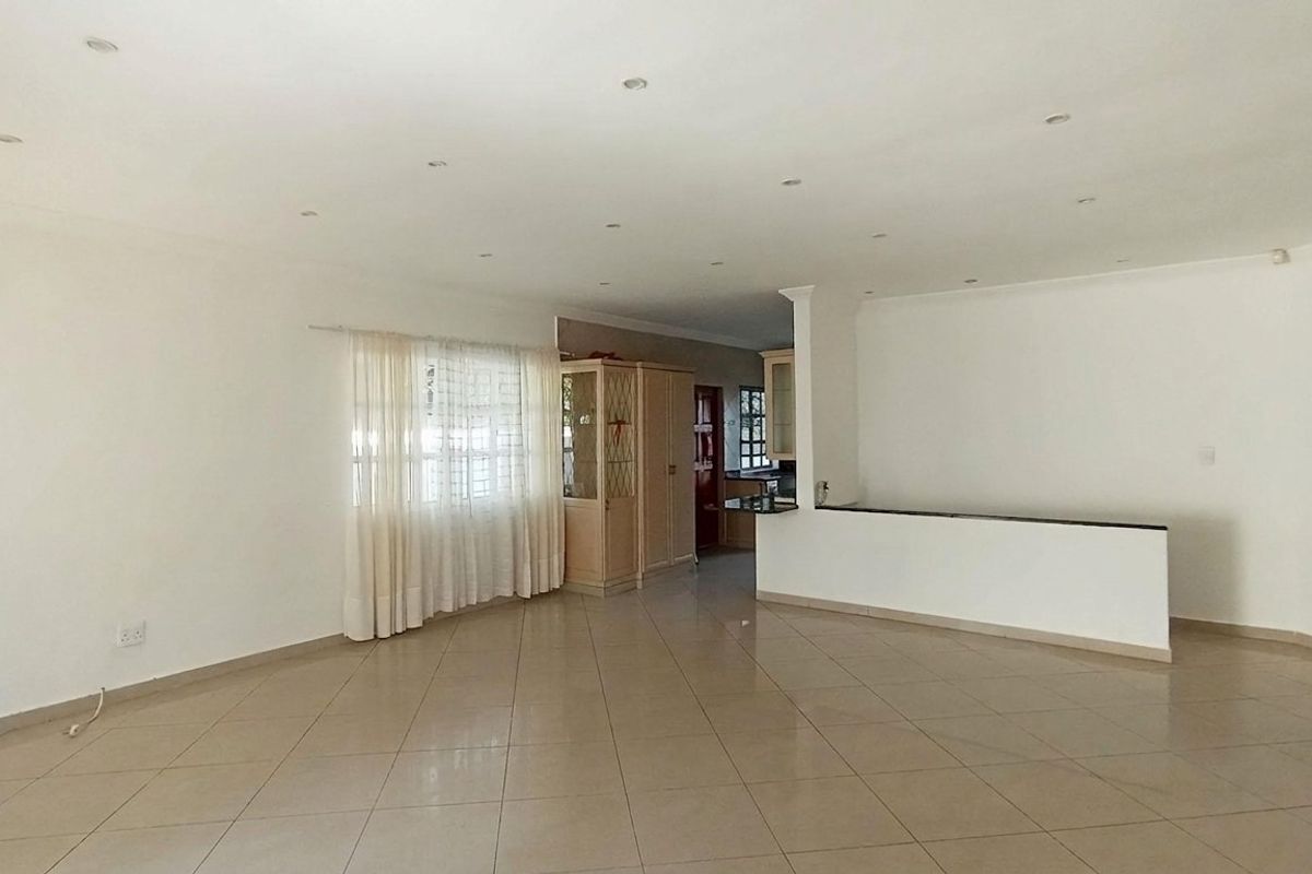 Spacious open-plan living area featuring tiled flooring, recessed ceiling lighting, and a partial partition wall leading to the kitchen space.
