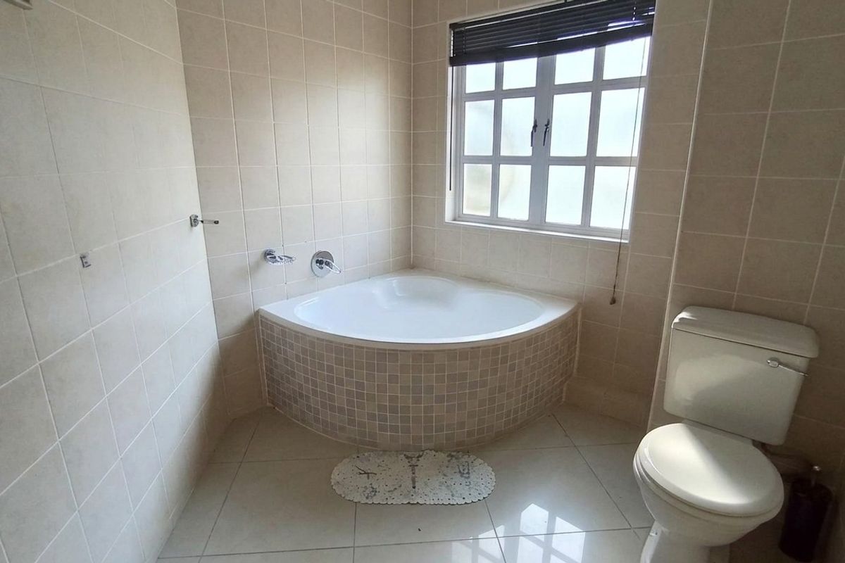 A functional bathroom featuring a corner bathtub with mosaic tiling, a standard toilet, and neutral wall tiles.