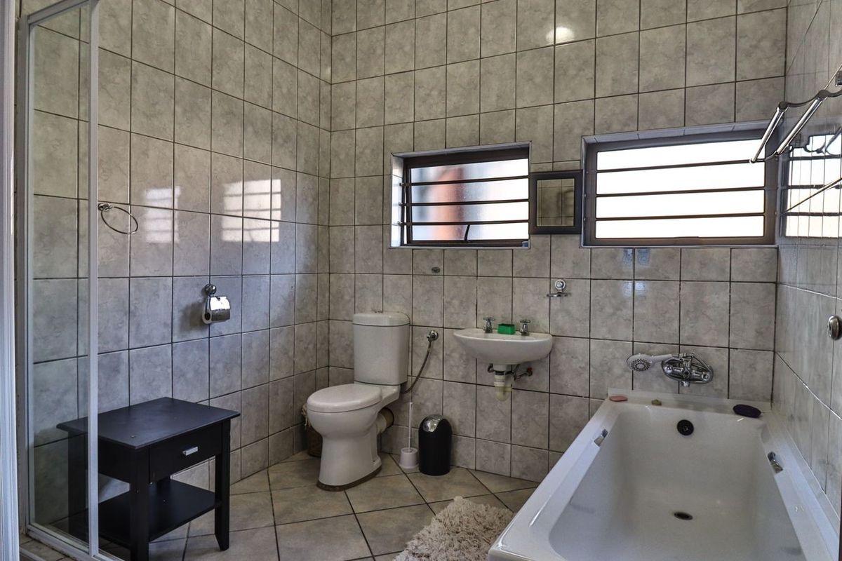 A functional bathroom featuring a bathtub, wall-mounted basin, toilet, and a separate glass-enclosed shower area with full-height wall tiling.