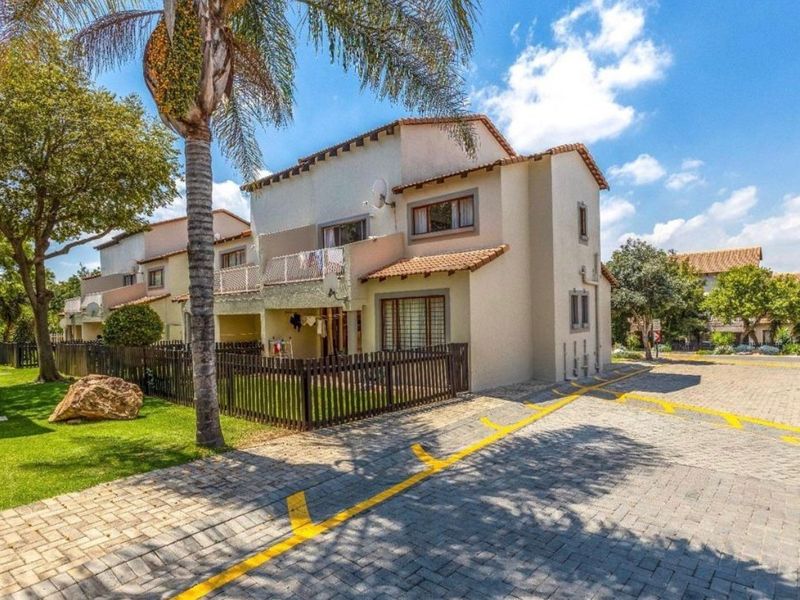 Exterior view of a multi-story apartment unit featuring a private fenced garden, balcony, and paved driveway access.