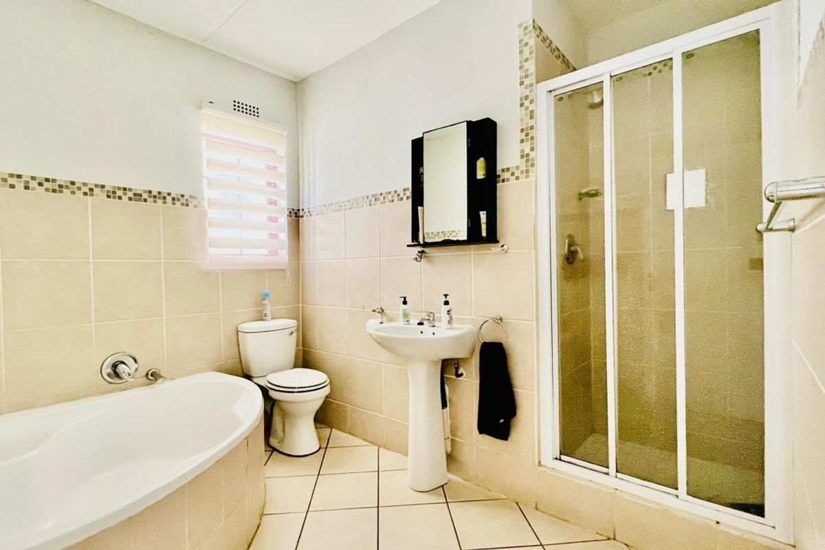 A functional bathroom featuring a corner bathtub, a separate glass-enclosed shower, a pedestal basin, and a toilet with neutral wall and floor tiling.