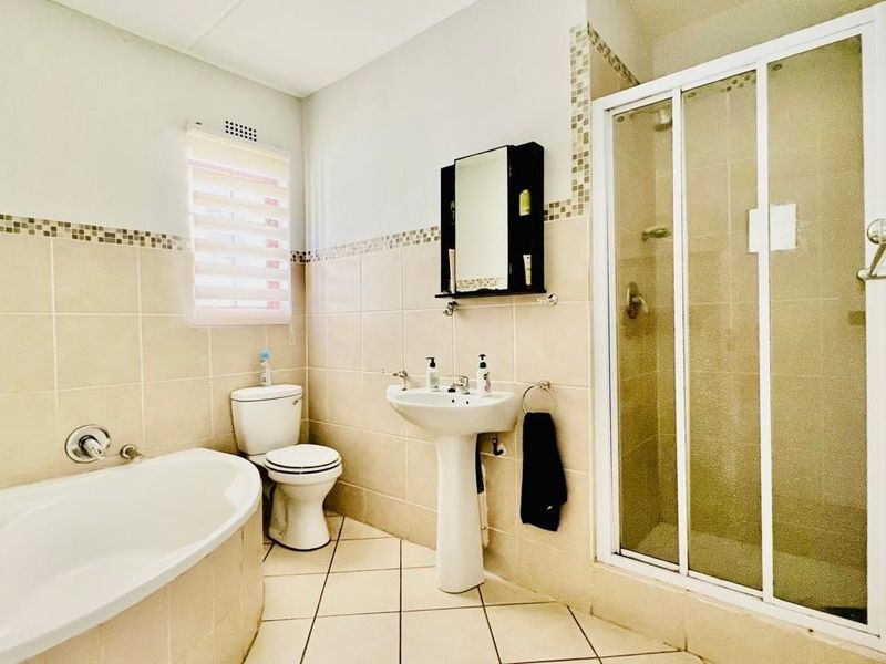 A functional bathroom featuring a corner bathtub, a separate glass-enclosed shower, a pedestal basin, and a toilet with neutral wall and floor tiling.