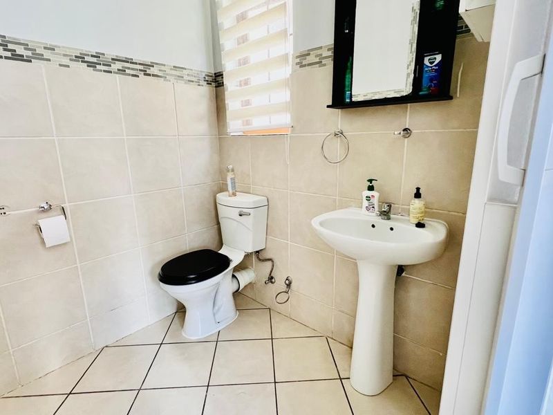 A functional bathroom featuring a pedestal sink, a standard toilet, and neutral wall tiling with a decorative mosaic border.
