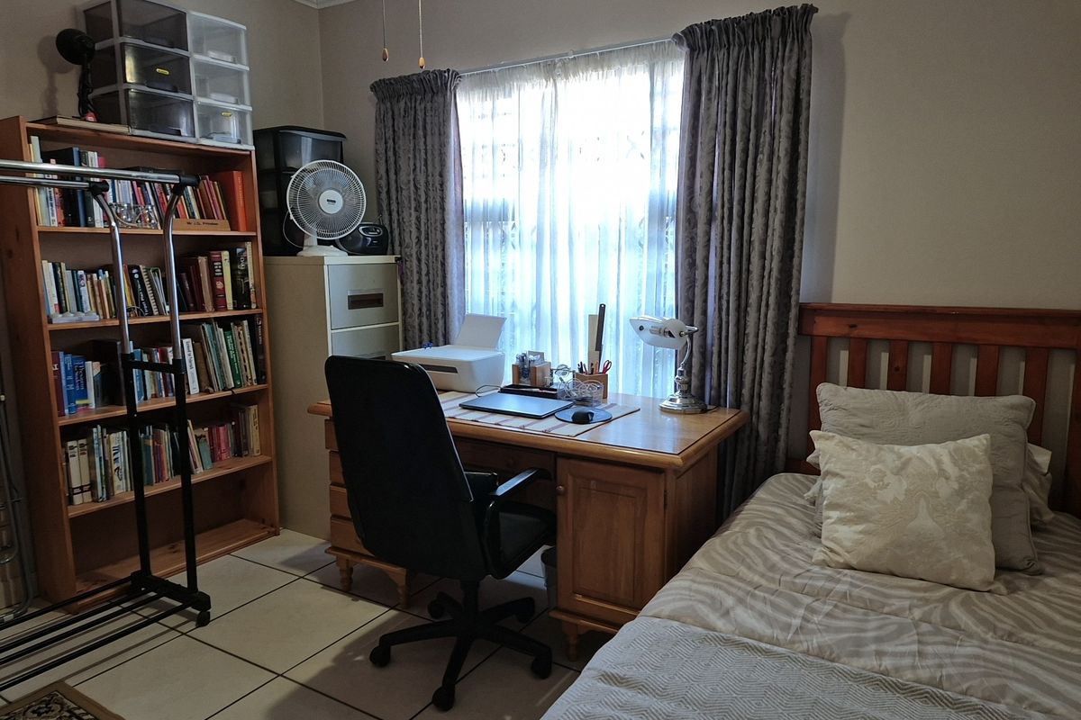 A functional bedroom featuring tiled flooring, a window with curtains, and crown molding, currently utilized as a home office and sleeping space.