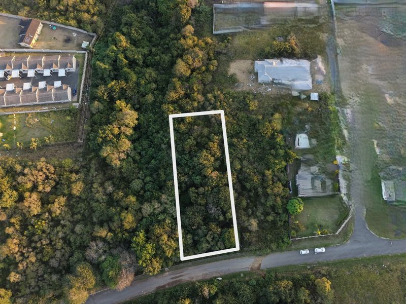 An aerial view of a vacant residential plot surrounded by dense vegetation and established neighborhood infrastructure.