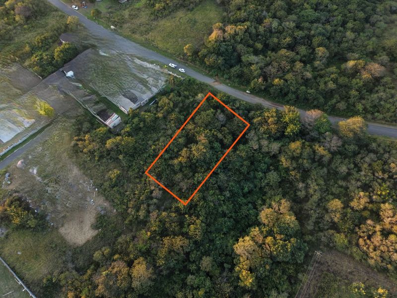 Aerial view of a vacant residential plot featuring dense natural vegetation and direct access to a nearby road.