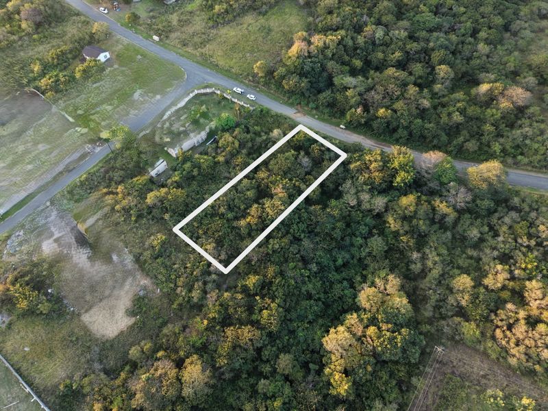 Aerial view of a vacant residential plot featuring dense natural vegetation and direct access to the adjacent road.