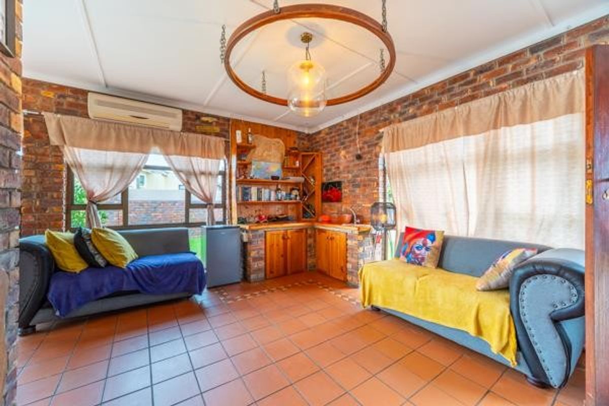 A rustic living area featuring exposed brick walls, terracotta floor tiles, a built-in wooden bar or prep area, and a ceiling-mounted feature light.