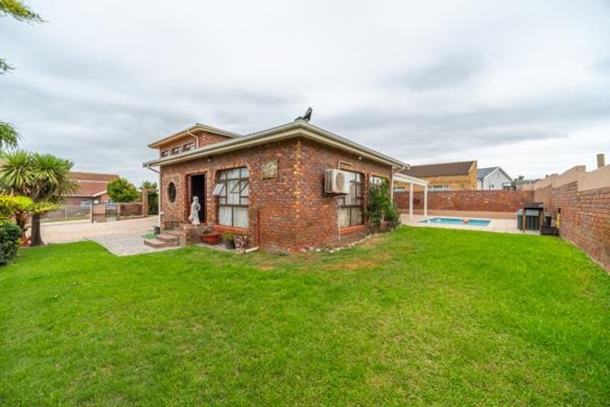 A rear view of a face-brick house featuring a swimming pool, paved patio area, and a spacious garden enclosed by a perimeter wall.