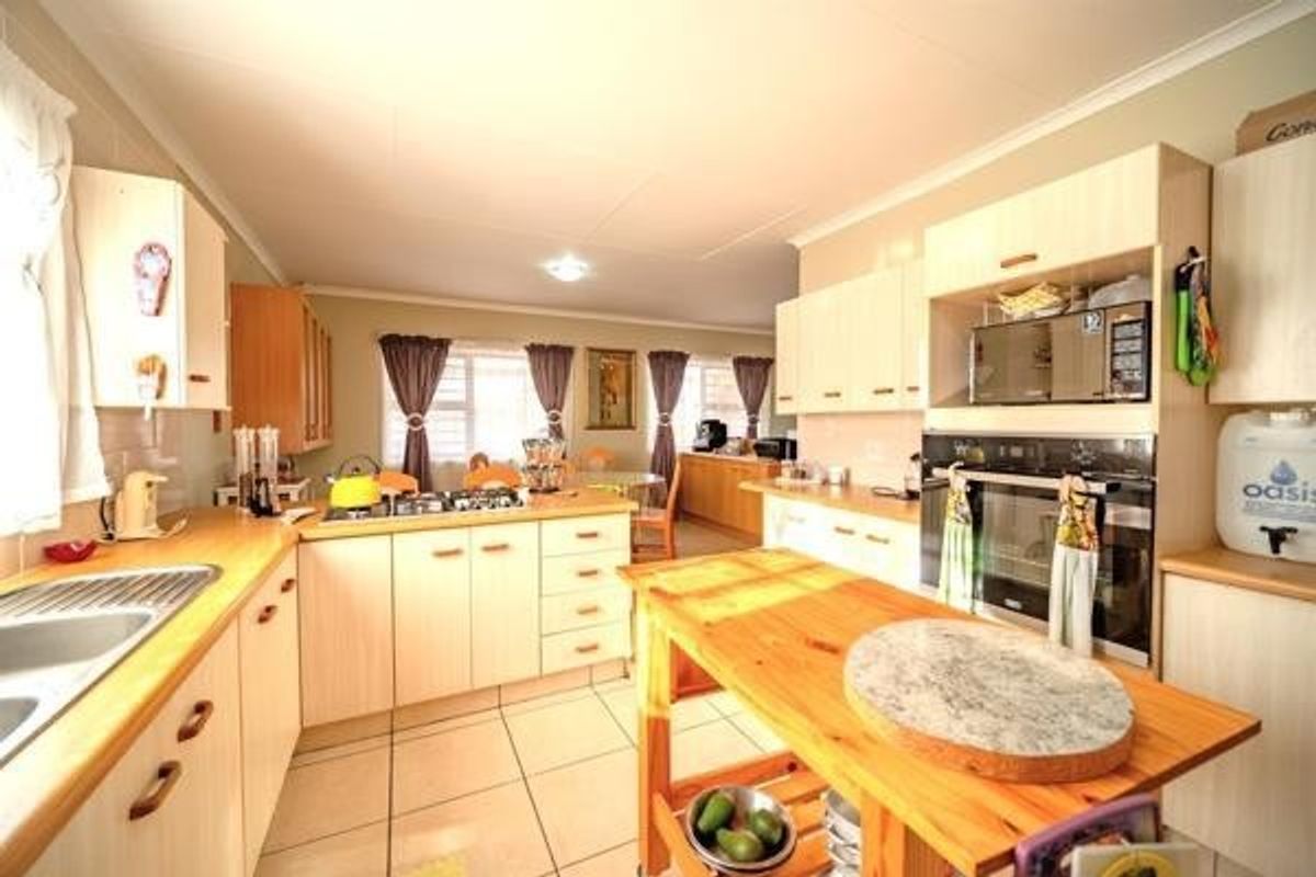 A functional kitchen featuring light-toned cabinetry, built-in oven, integrated microwave, and a central wooden island, opening into a dining area with tiled flooring.