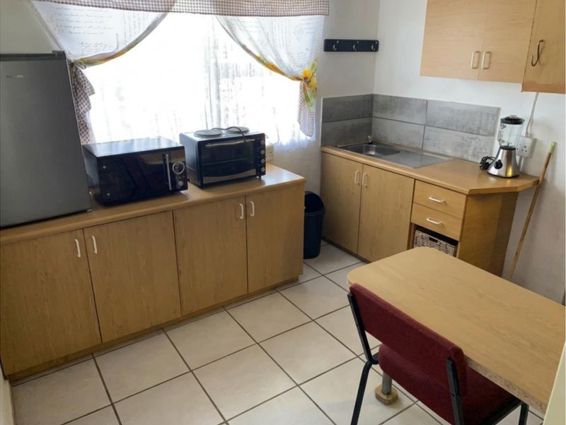 A compact kitchen featuring laminate cabinetry, a stainless steel sink, tiled splashback, and ceramic floor tiles.