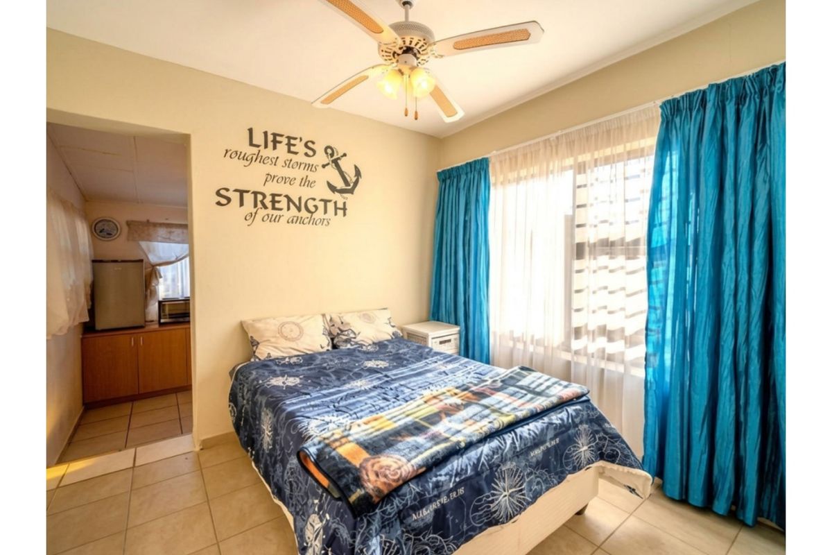 A bedroom featuring tiled flooring and a ceiling fan, with an adjoining space visible through the doorway.