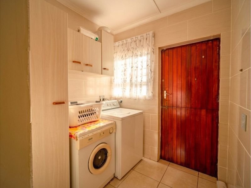 A functional laundry room featuring tiled walls and flooring, built-in cabinetry for storage, and a solid timber exterior door.
