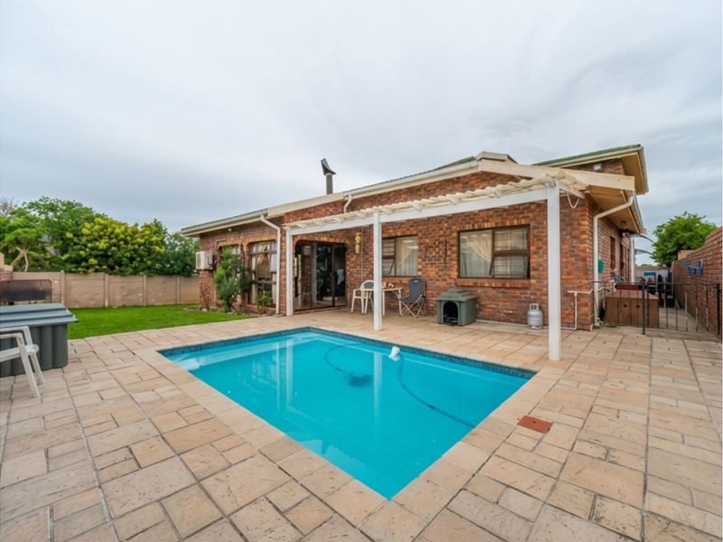 Rear exterior view featuring a swimming pool, paved patio area, and a pergola attached to the brick house structure.