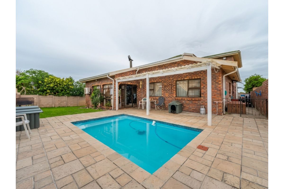 Rear exterior view featuring a swimming pool, paved patio area, and a pergola attached to the brick house structure.
