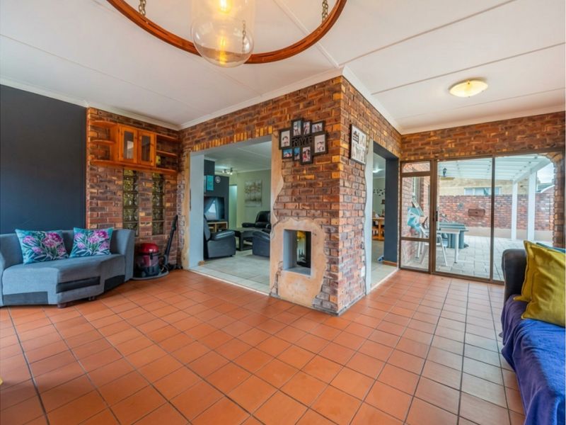 Open-plan living area featuring exposed brick walls, terracotta tiling, and a central fireplace, with direct access to an outdoor patio through sliding glass doors.