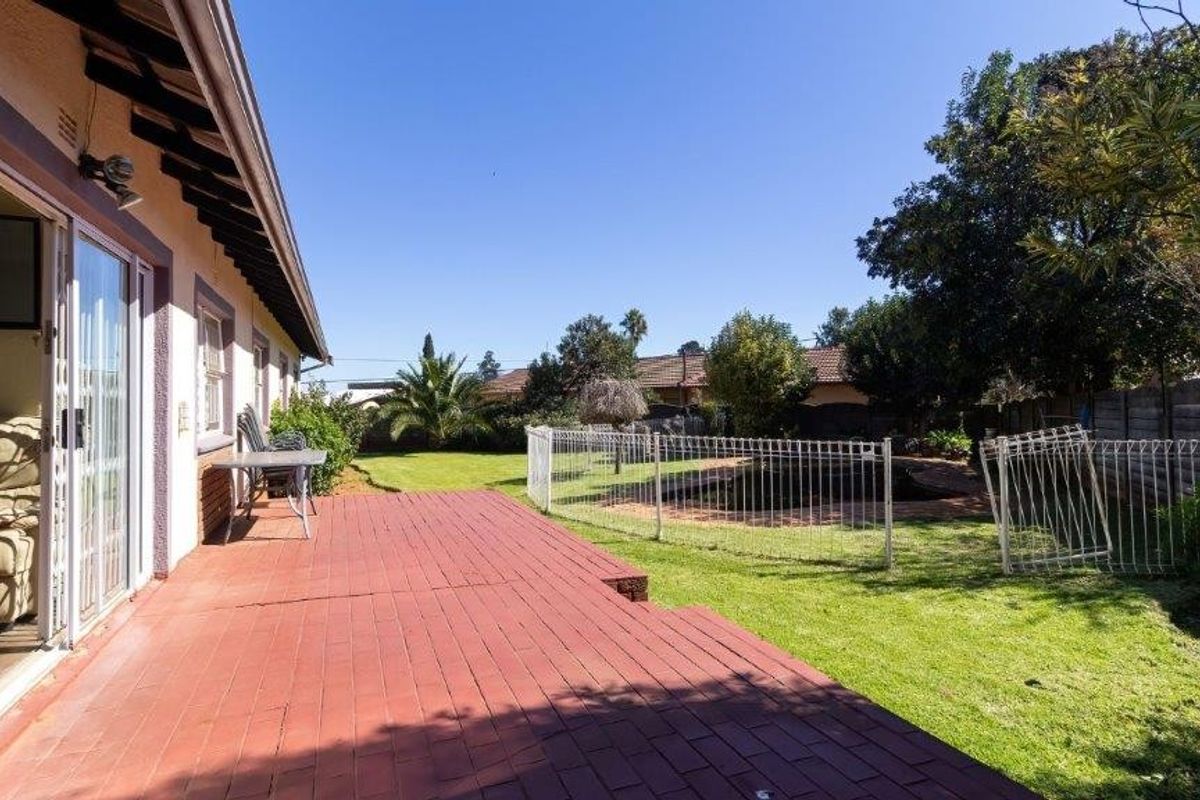 A rear exterior view featuring a paved patio area, a lawned garden, and a fenced pool area.