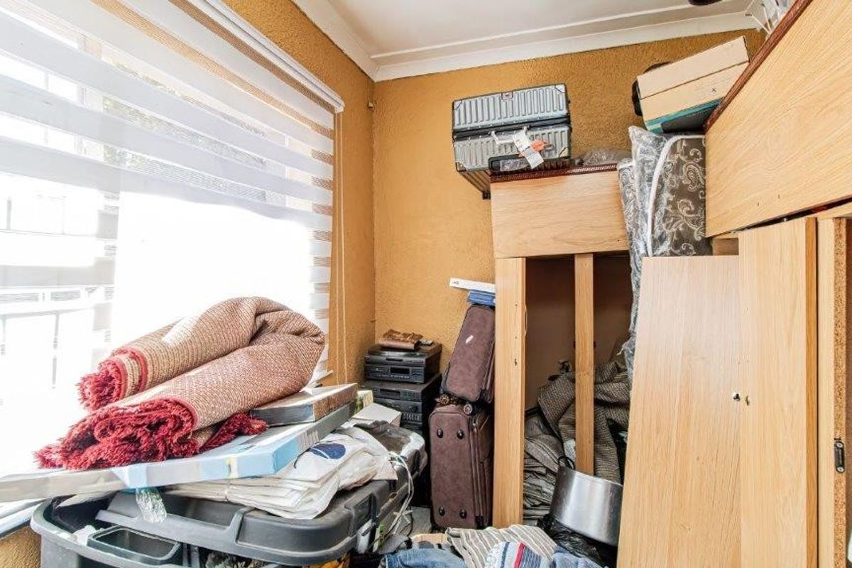 A bedroom space featuring a window with fitted blinds and built-in cabinetry, currently used for storage.