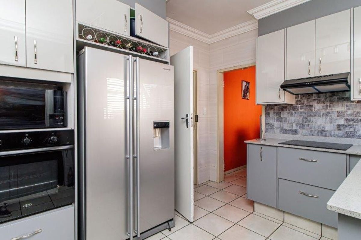 Modern kitchen featuring grey cabinetry, stone countertops, tiled backsplash, built-in oven, microwave, and extractor fan with tiled flooring.