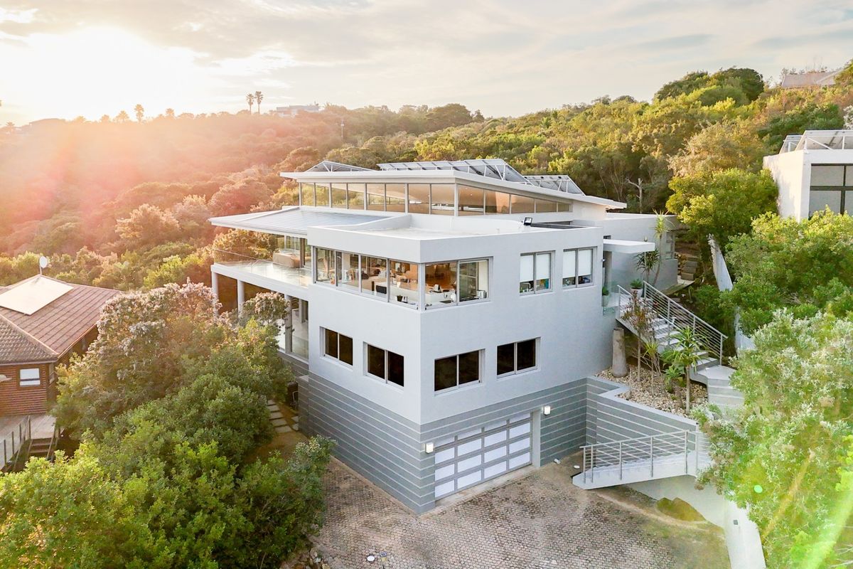 Aerial view of a modern multi-level residence featuring solar panels, a double garage, paved driveway, and expansive balconies set in a lush landscape.