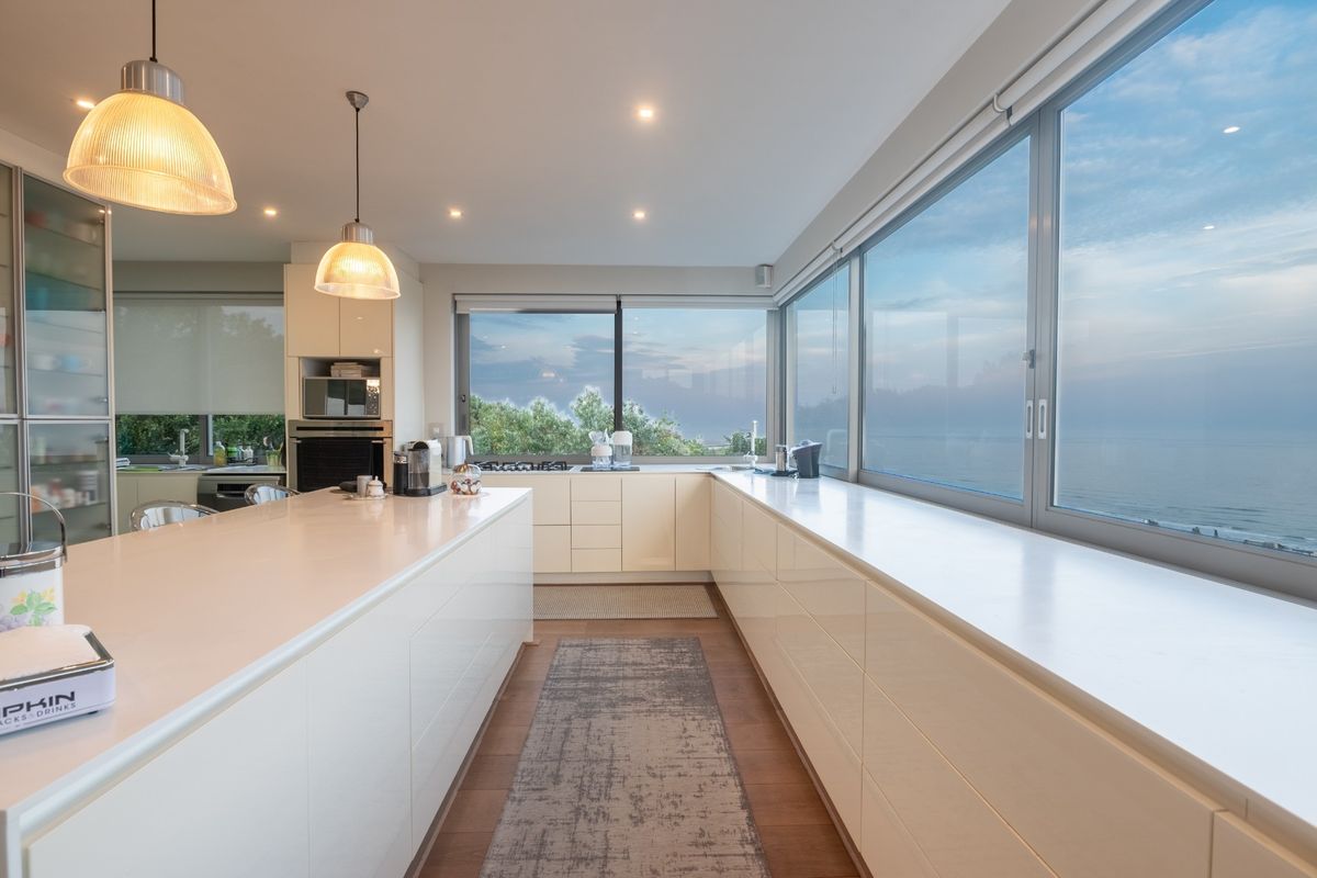 Modern, high-end kitchen featuring a large island, sleek cabinetry, built-in appliances, and expansive windows offering panoramic ocean views.