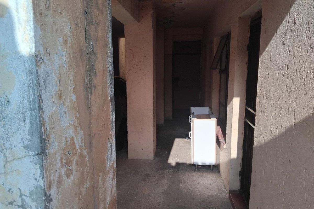 A covered exterior walkway or corridor showing significant signs of wear, including peeling paint and weathered concrete surfaces.