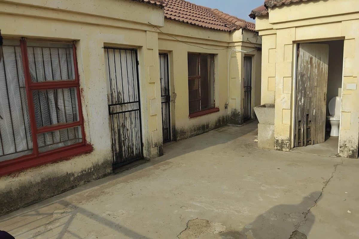 Exterior view of an apartment complex courtyard featuring concrete paving, multiple entry doors with security gates, and visible signs of exterior wear and maintenance needs.