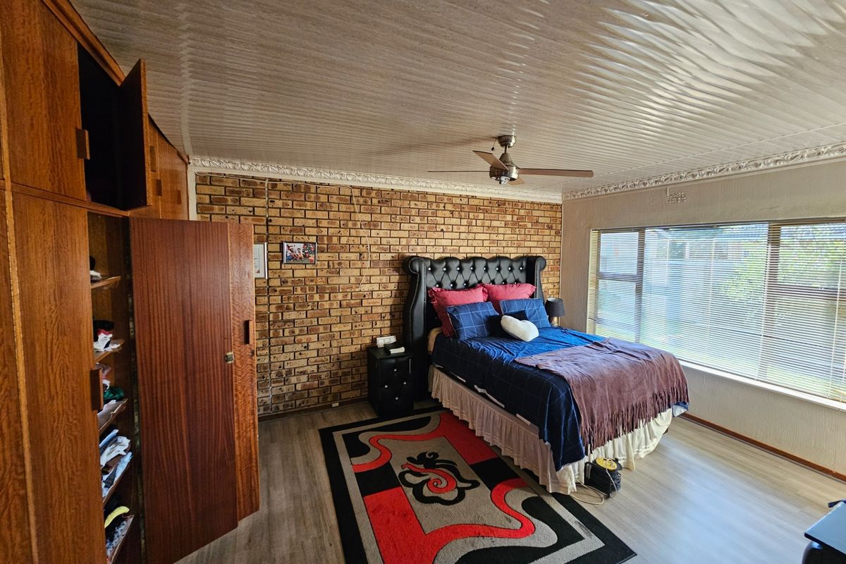 Spacious bedroom featuring an exposed brick feature wall, built-in wooden cabinetry, a ceiling fan, and large windows providing natural light.