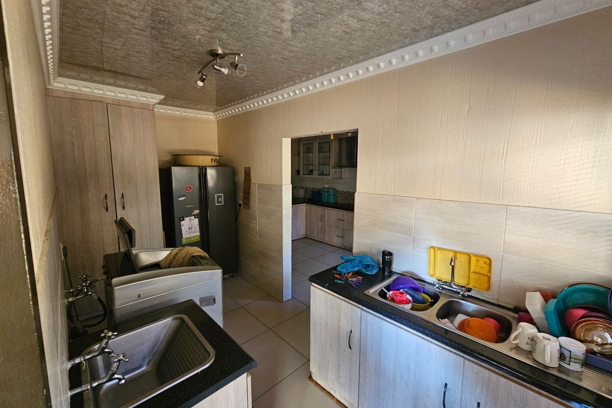 Functional kitchen area featuring dual sink stations, laminate cabinetry, granite countertops, and tiled splashbacks with a connected scullery or secondary prep area.
