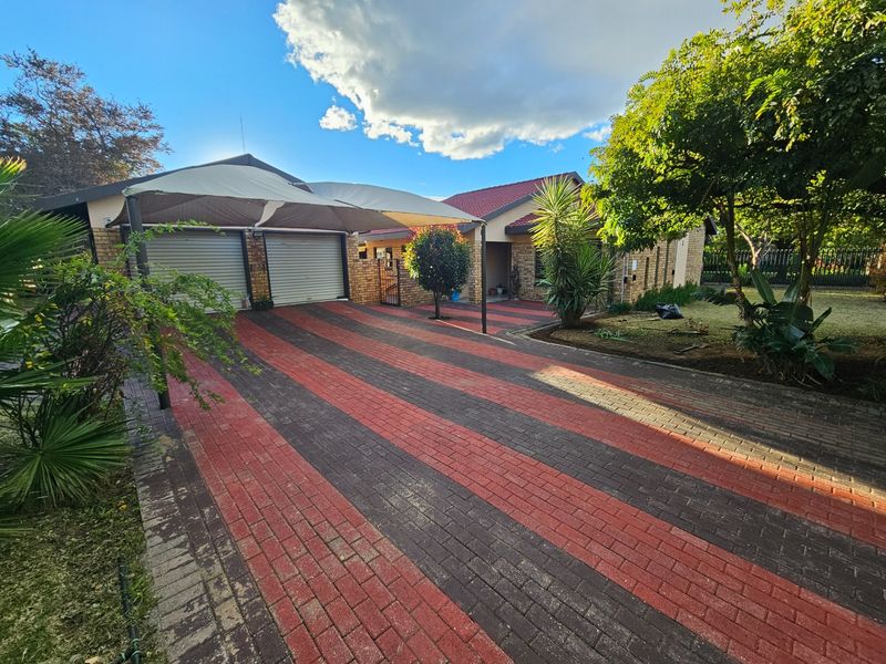 Front exterior view of the property featuring a paved driveway, double garage with a shade sail carport, and established garden landscaping.