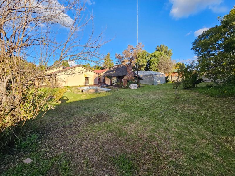 Spacious rear garden featuring a swimming pool, a traditional thatched lapa with a built-in brick braai, and established lawn area.
