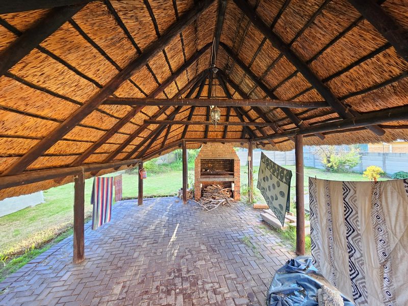 Covered outdoor patio featuring a traditional thatched roof, brick fireplace, and paved flooring, offering a rustic space for outdoor entertaining.