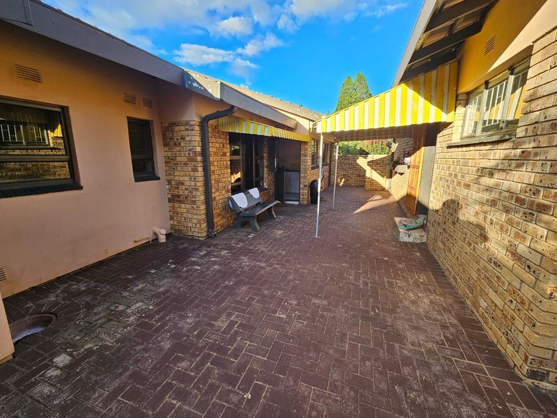 A paved rear courtyard area featuring facebrick walls and a retractable yellow and white striped awning providing shade.