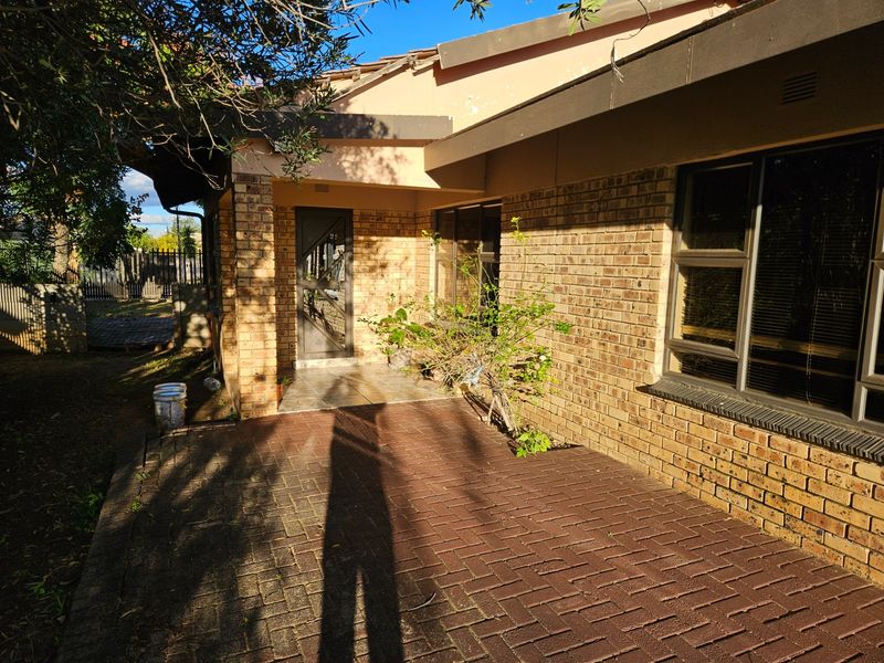 Rear exterior view of a face brick house featuring a paved patio area, aluminium window frames, and a tiled entrance porch.