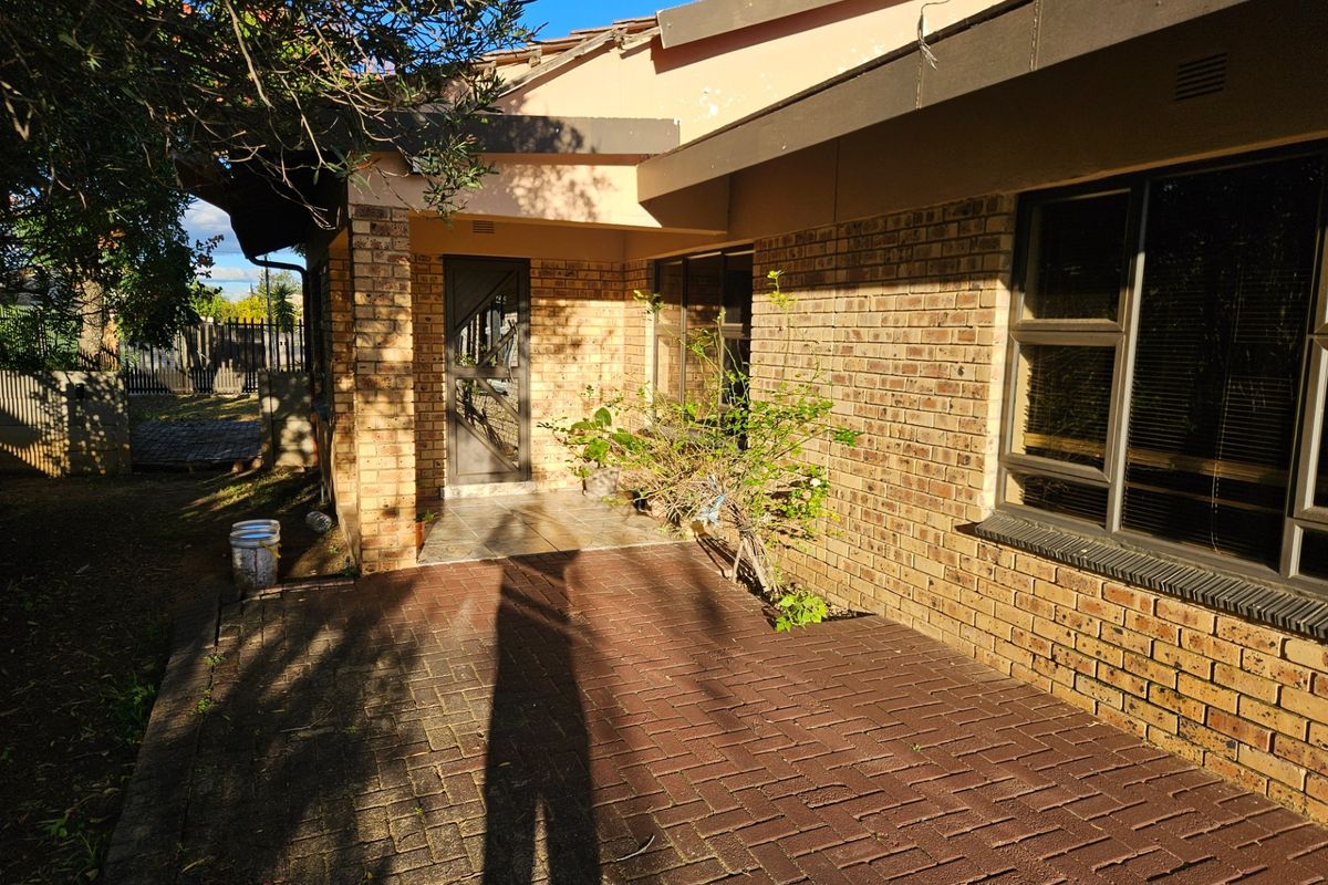 Rear exterior view of a face brick house featuring a paved patio area, aluminium window frames, and a tiled entrance porch.