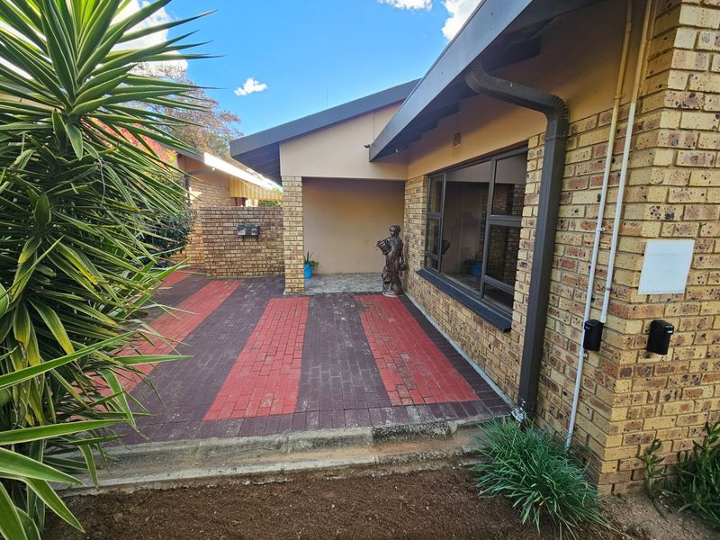 A rear exterior view featuring a covered patio area with brick paving and face brick wall finishes.