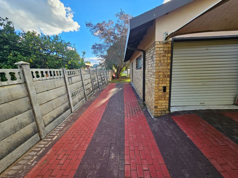 A side exterior view featuring patterned brick paving, a precast concrete boundary wall, and a roller garage door with an overhead shade sail.