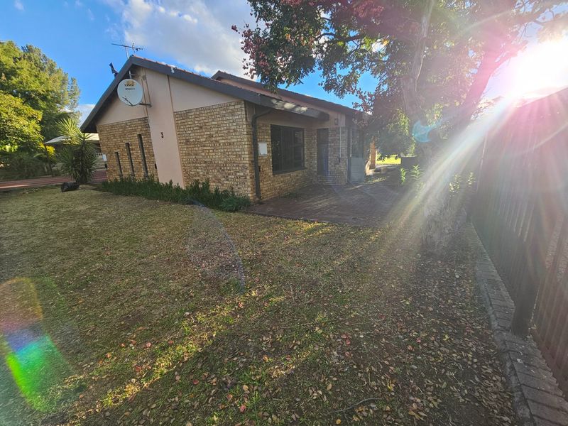 Rear view of the property featuring a face brick facade, paved patio area, and surrounding garden space.