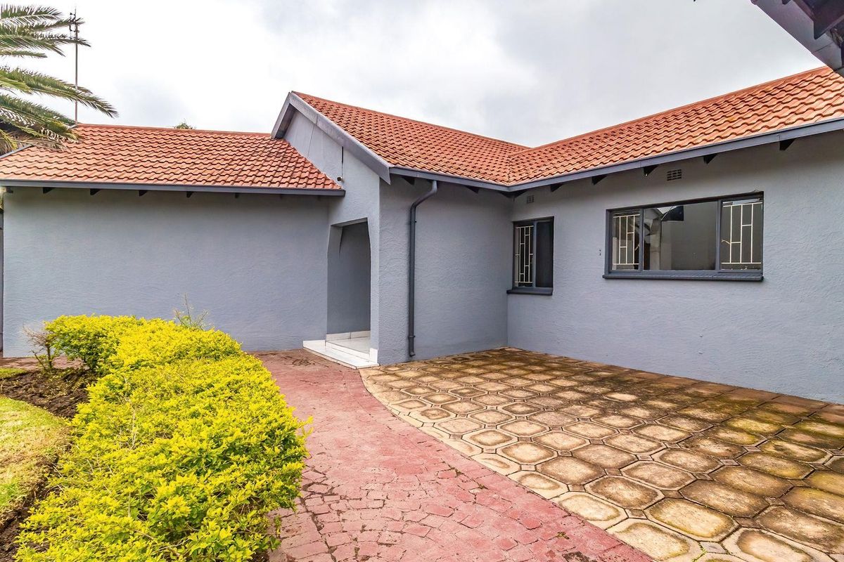 A view of the rear exterior of the house featuring a paved patio area, tiled roof, and landscaped garden access.